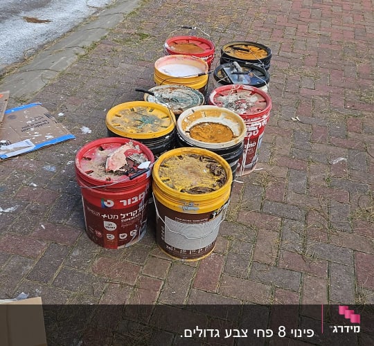 דלי צבעים ריקים על מדרכה ליד פח ירוק